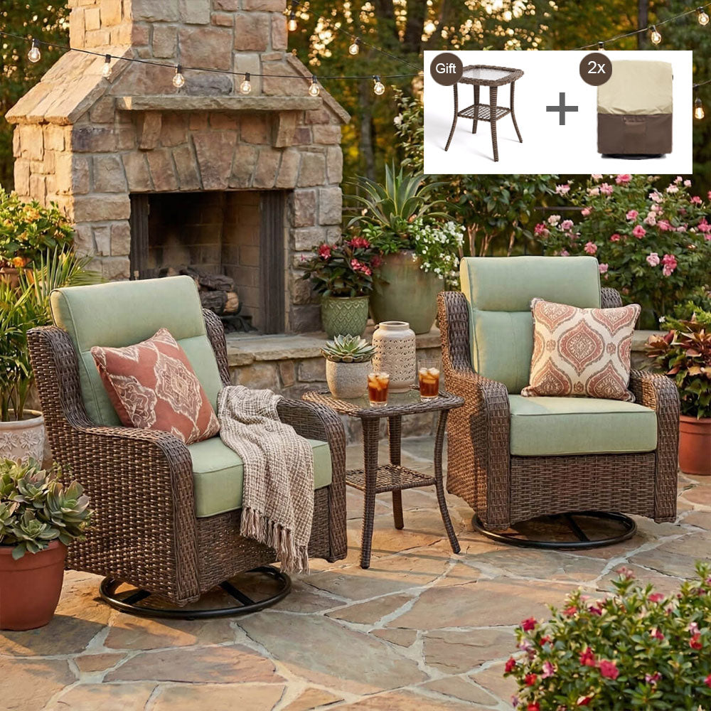 Outdoor patio furniture set with two brown wicker swivel armchairs, light sage green cushions, patterned throw pillows, and a matching small round side table. The chairs are arranged on a stone patio in front of a stone fireplace, with garden plants and flowers in the background.