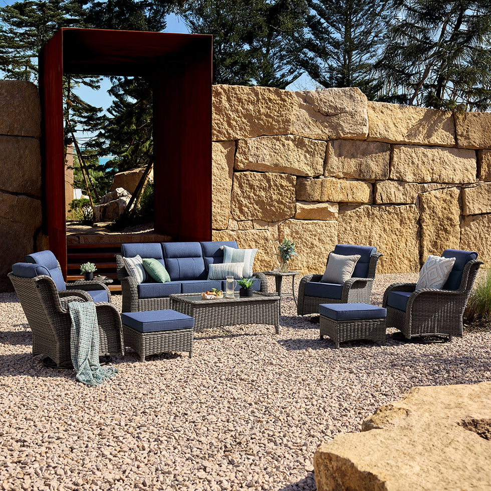 Outdoor patio sofa set with wicker furniture against a stone wall.