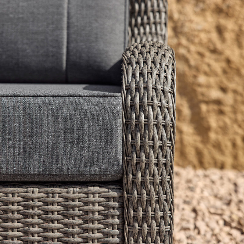 Gray cushioned outdoor furniture with wicker armrests against a textured wall.