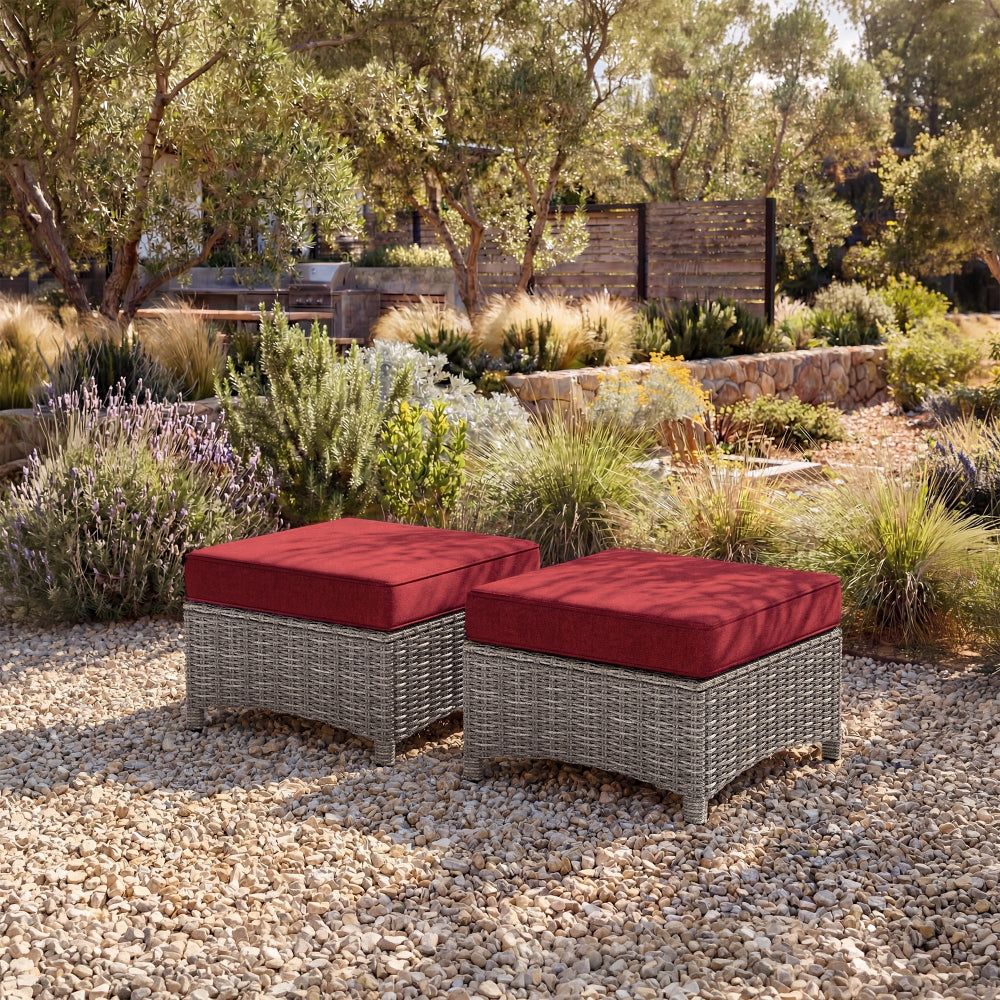 Two wicker ottomans with red cushions in a garden setting.