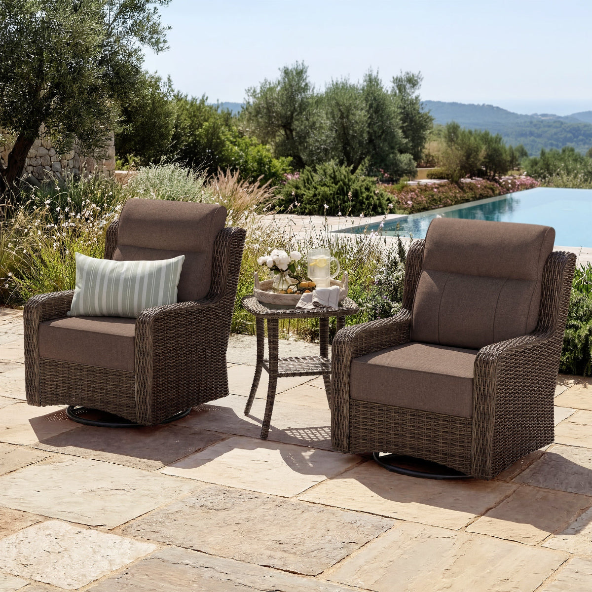 Two wicker chairs with cushions on a patio by a poolside with a scenic background.