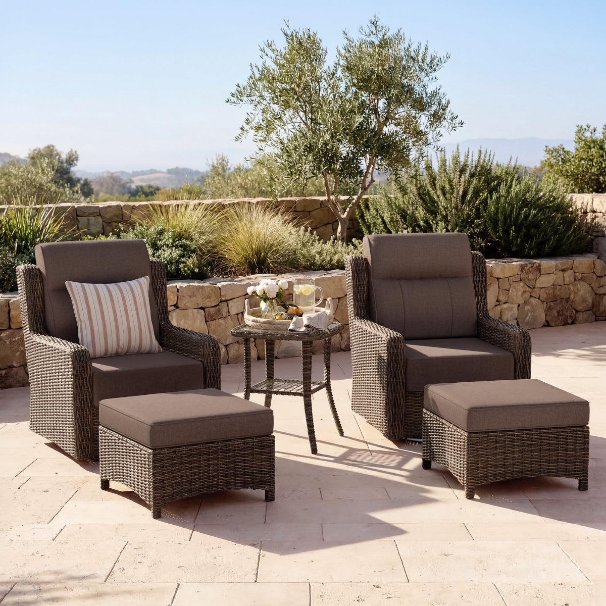 Outdoor brown wicker patio furniture set with chairs, ottomans, and a small table on a stone patio.