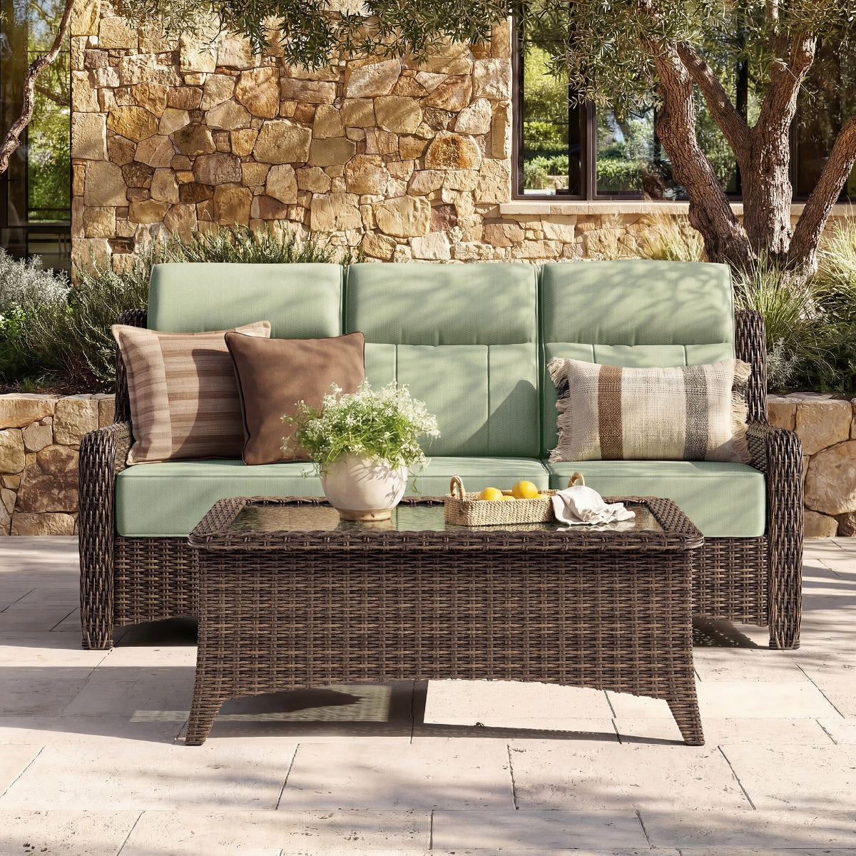 Outdoor patio set with green cushions and a wicker table in front of a stone wall.